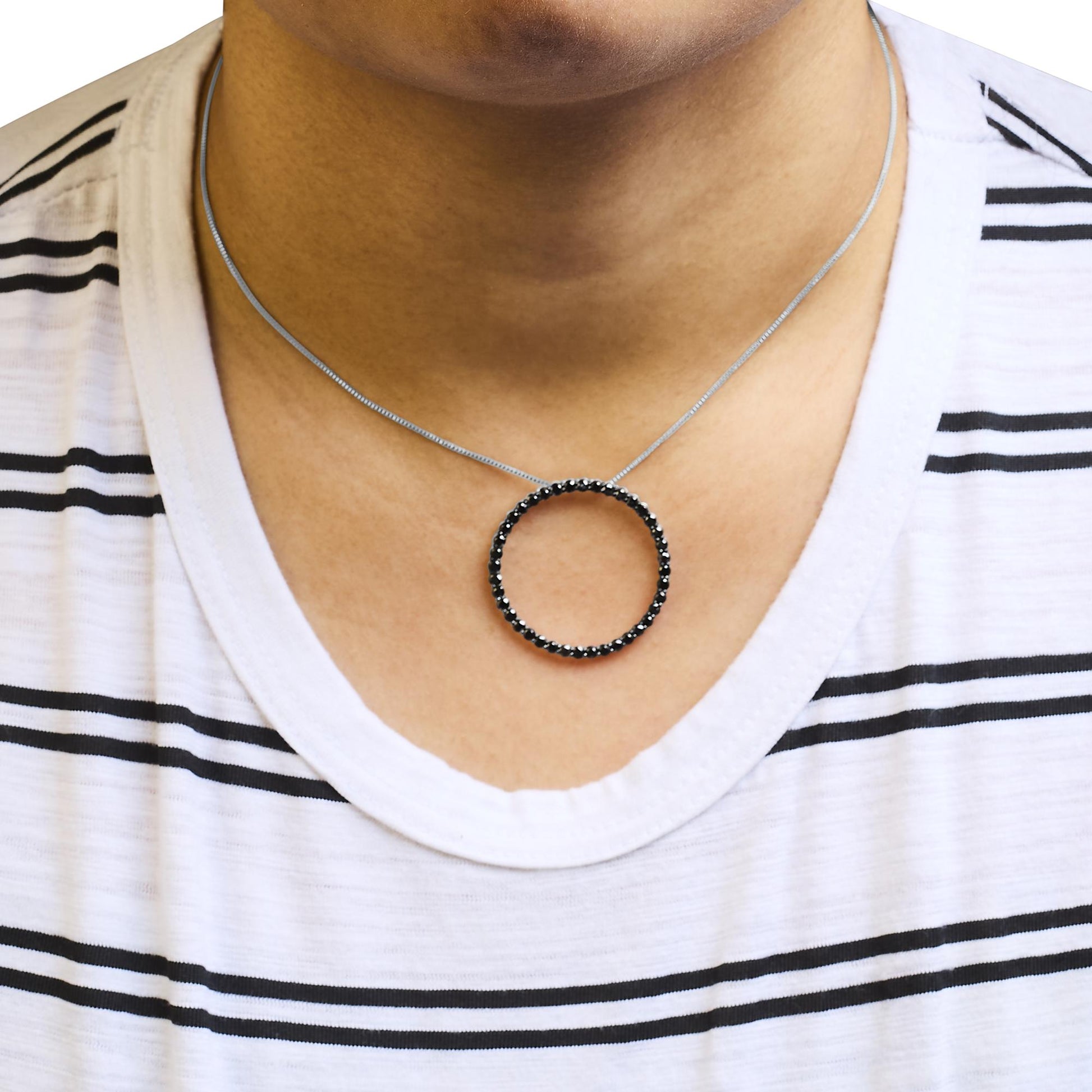 Close-up front view of a white necklace with a circular pendant featuring round black gemstones in a shared prong setting, worn on a model with a white and black striped shirt.