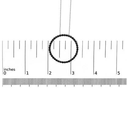 Pendant necklace with a circular design of round black gemstones in shared prong setting, displayed on a ruler for size reference, shot from the front.