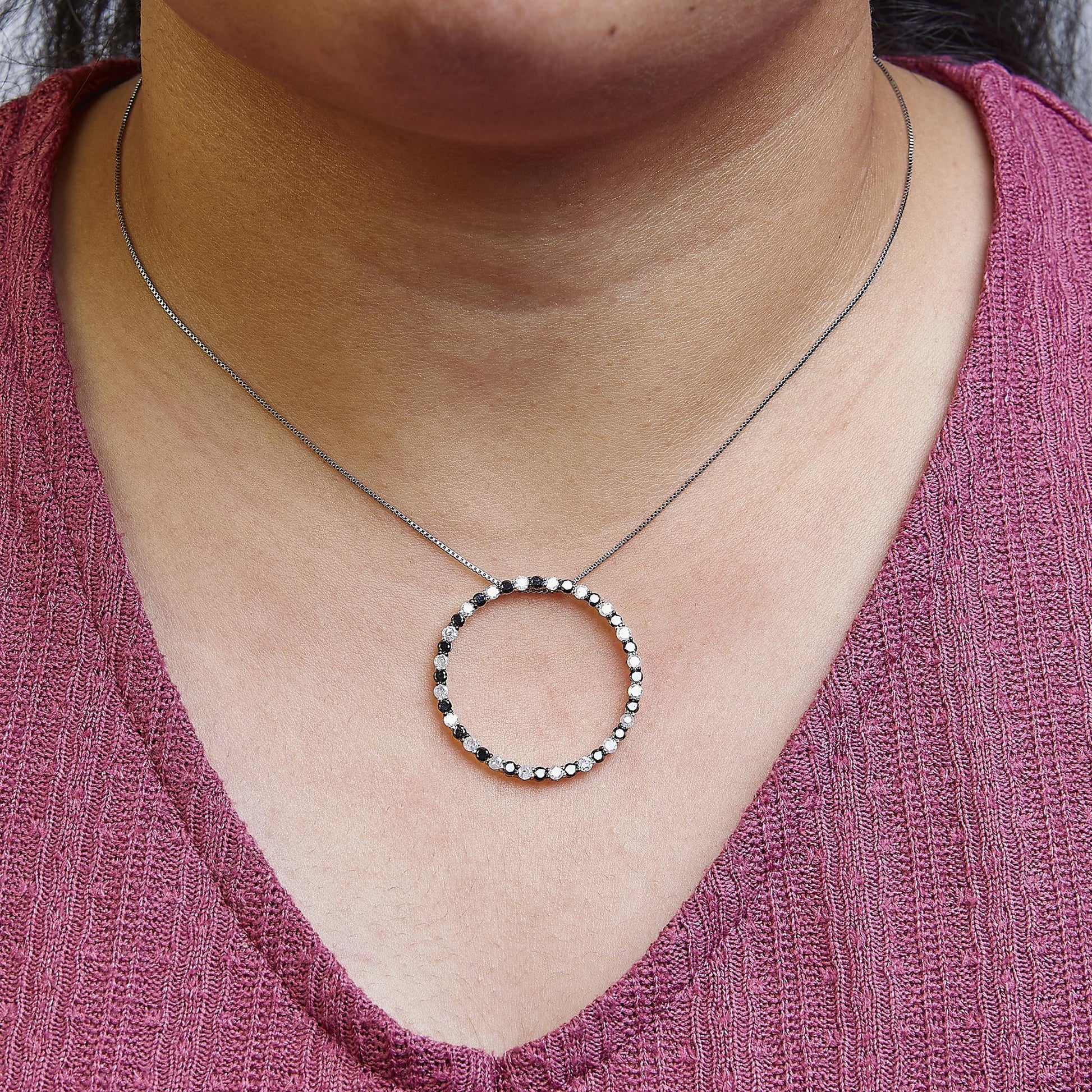 Close-up front view of a white metal necklace with a circular pendant featuring alternating round black and white gemstones in prong settings, worn on a model with a pink textured top.