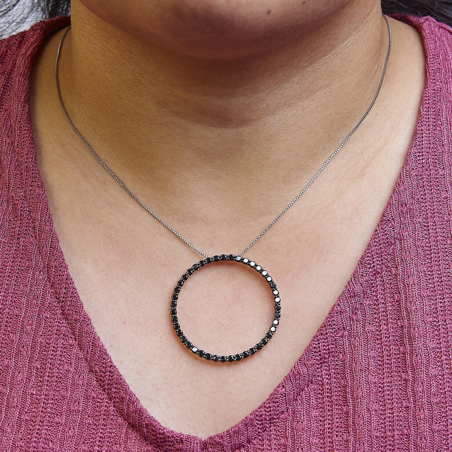 Front-facing close-up of a white metal necklace with a large circular pendant featuring black round gemstones, worn on a model.