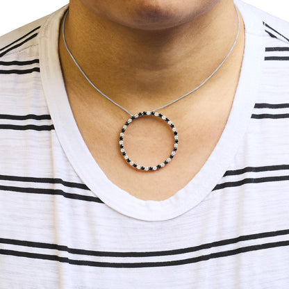 White metal necklace with a circular pendant featuring alternating black and white round gemstones in prong settings, worn on a model, front-facing angle.