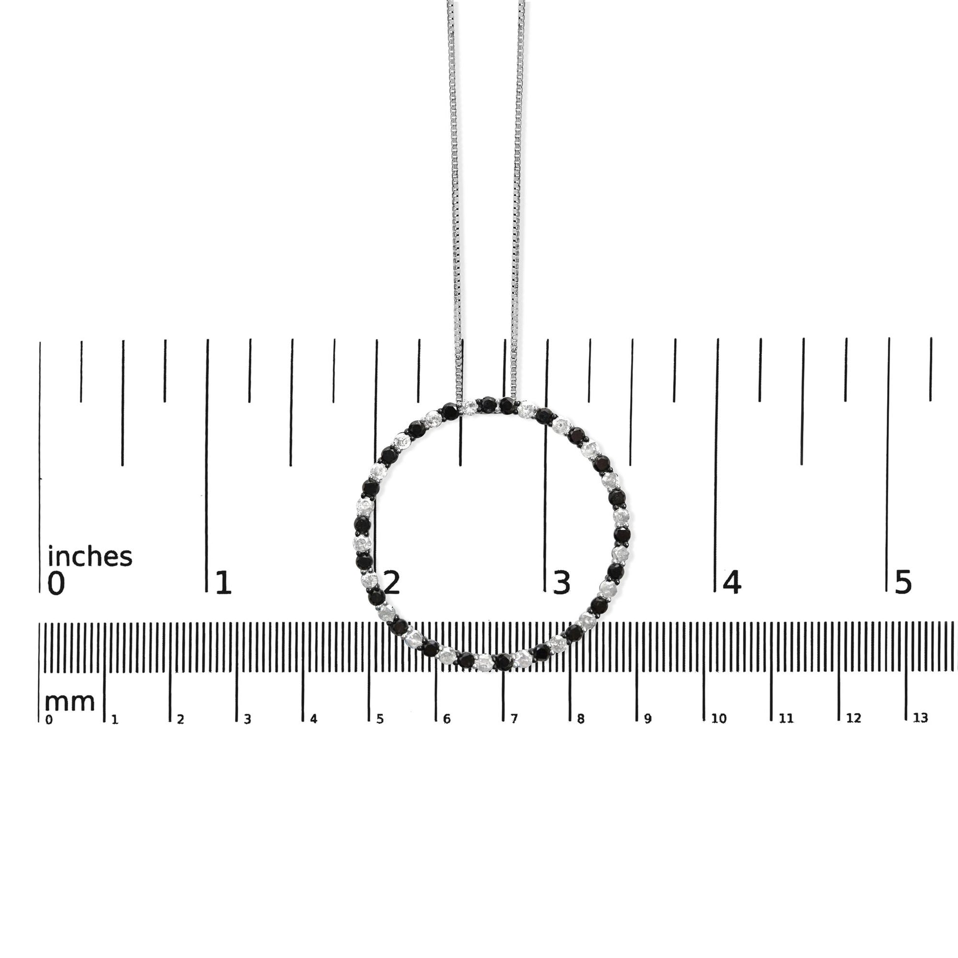 Front view of a white metal circle necklace with alternating black and white round gemstones in prong settings, displayed on a ruler for size reference.