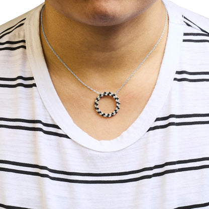 Front-facing close-up of a white metal necklace with a circular pendant featuring alternating black and white round gemstones, worn on a model with a white and black striped shirt.