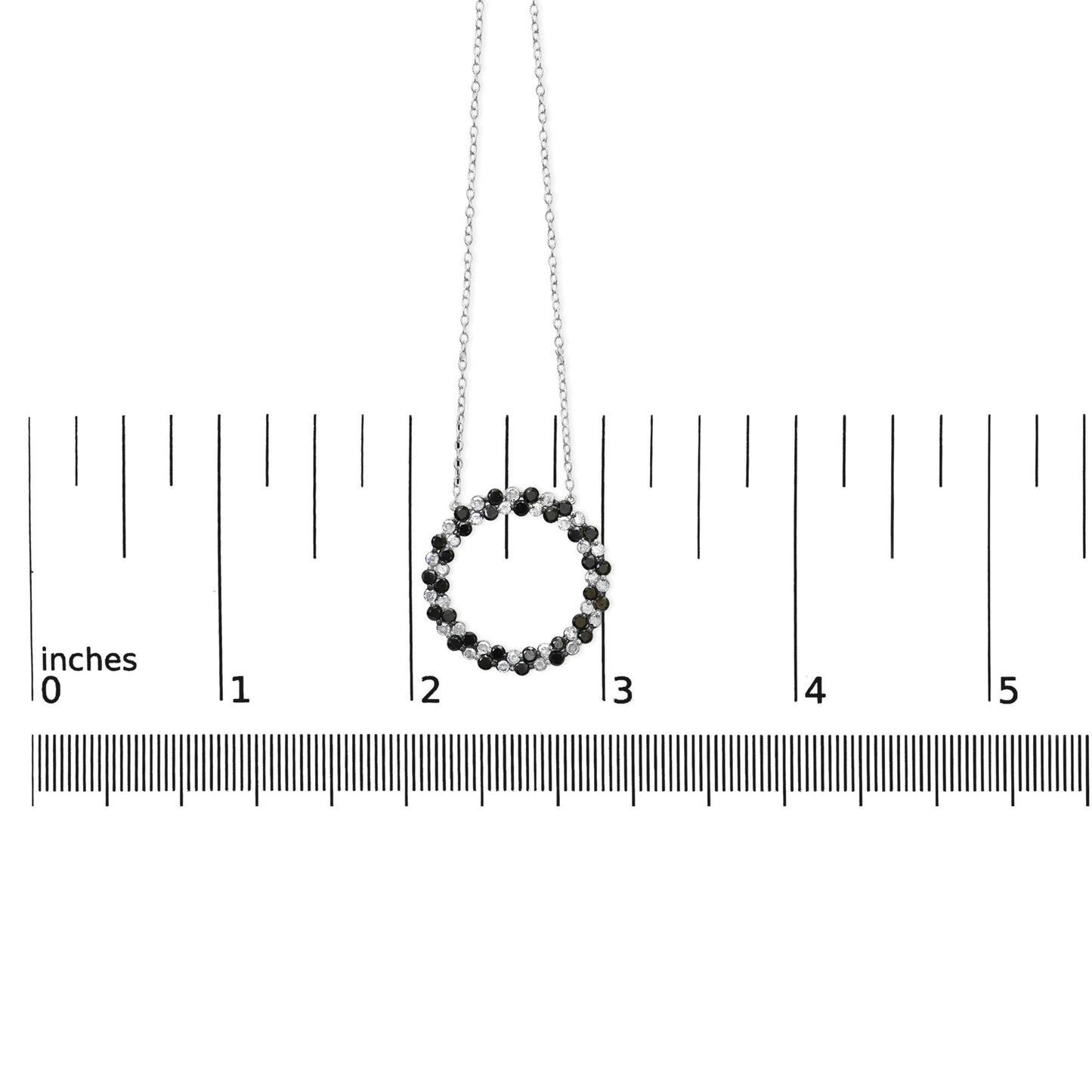 Front view of a white necklace pendant in a circular shape with alternating black and white round gemstones in prong settings, shown on a ruler for size reference.