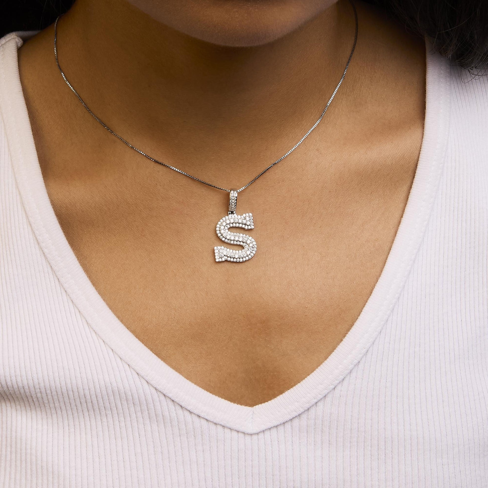 White metal necklace with an 'S' shaped pendant encrusted with round white gemstones in prong settings, shown worn on a model from the front angle.