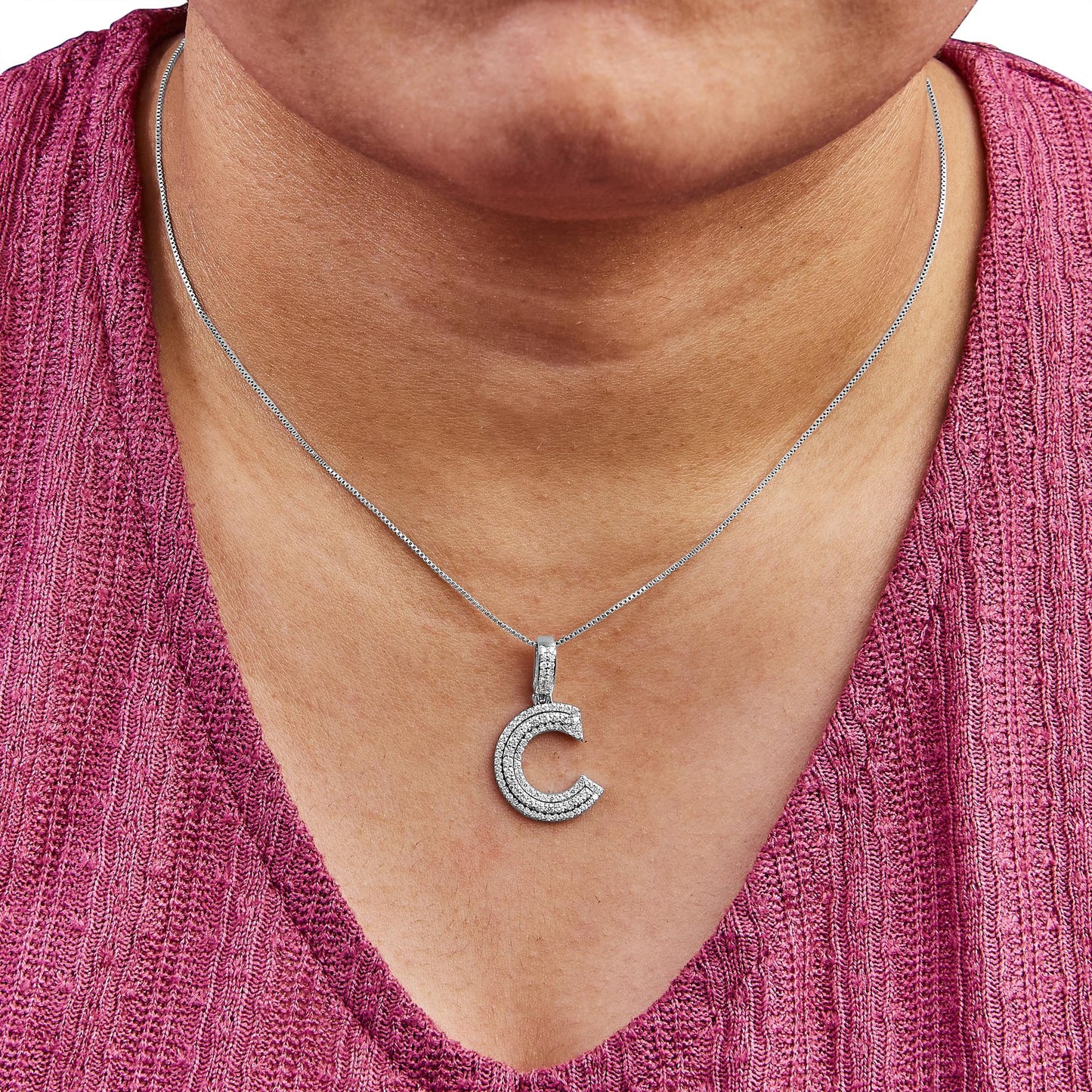 Close-up front view of a person wearing a white metal necklace with a 'C' shaped pendant adorned with multiple rows of small white gemstones.