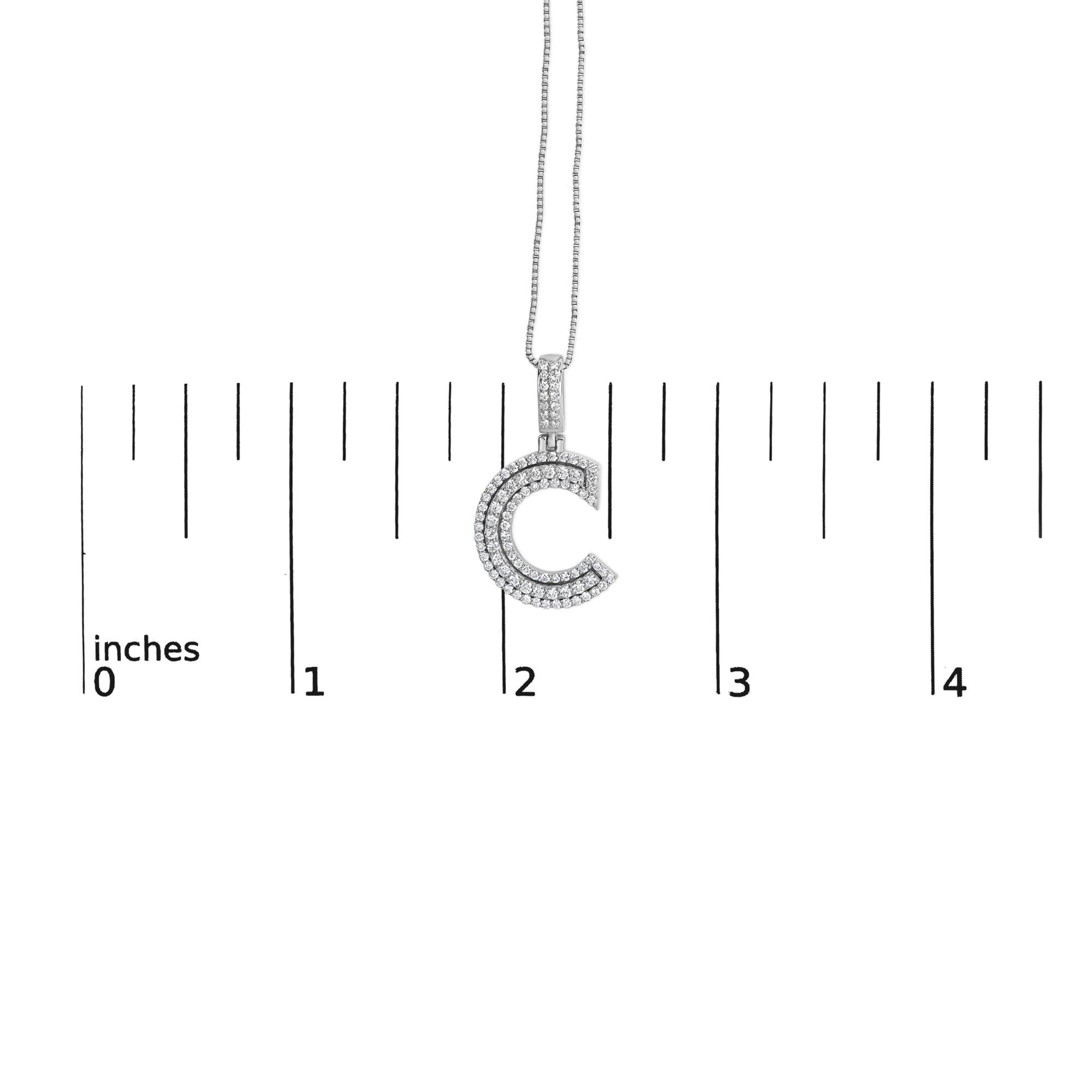 Front view of white metal necklace with C-shaped pendant covered in two rows of round white gemstones, photographed on a ruler for size reference.