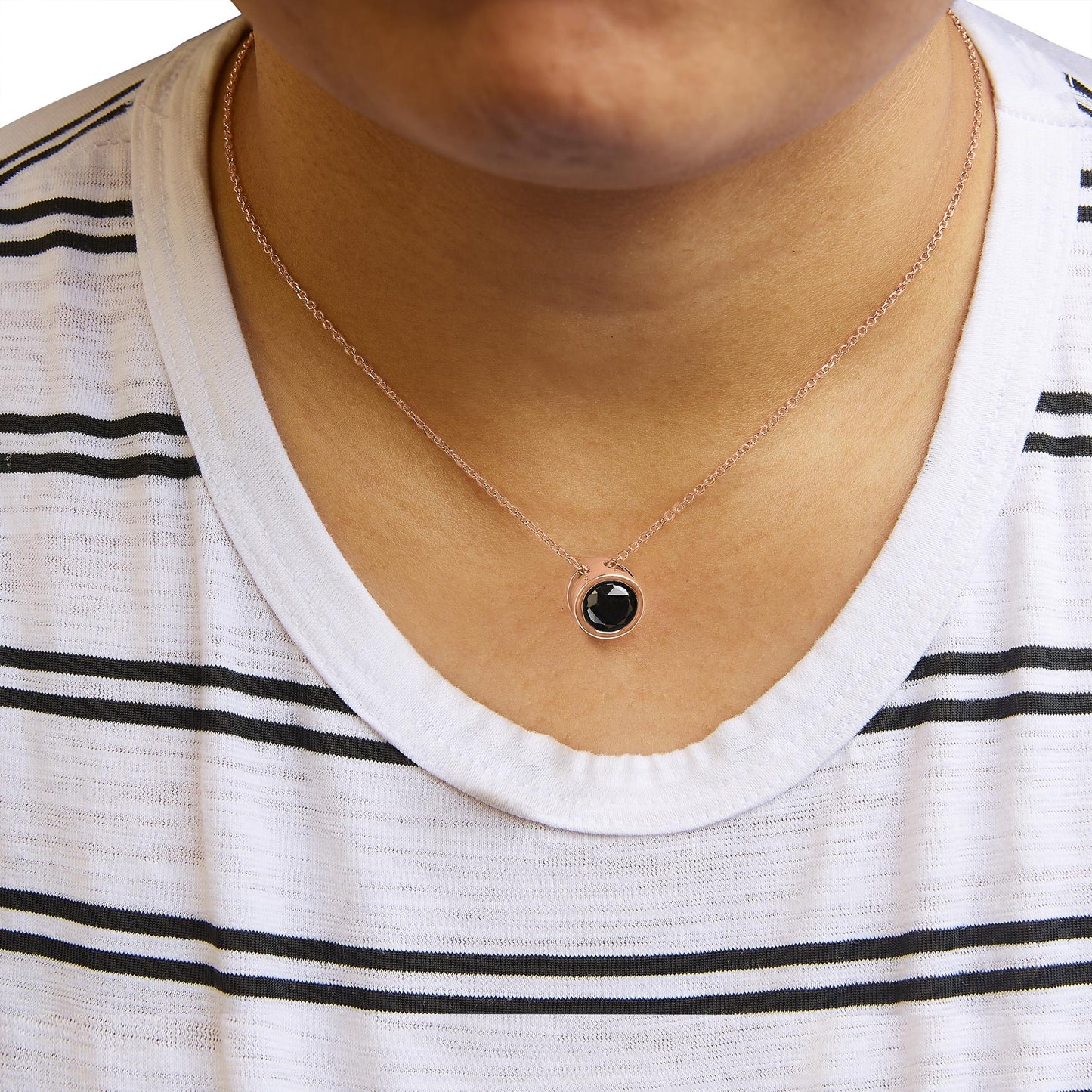 Close-up front view of a rose-colored necklace with a round black gemstone in a bezel setting, worn on a model with a white and black striped shirt.