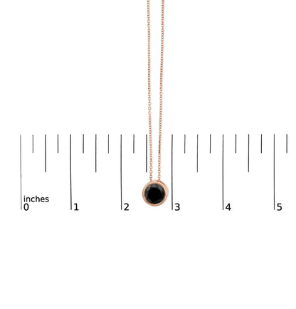 Rose metal necklace with round black gemstone in bezel setting, hanging vertically above a ruler for size reference, front view.