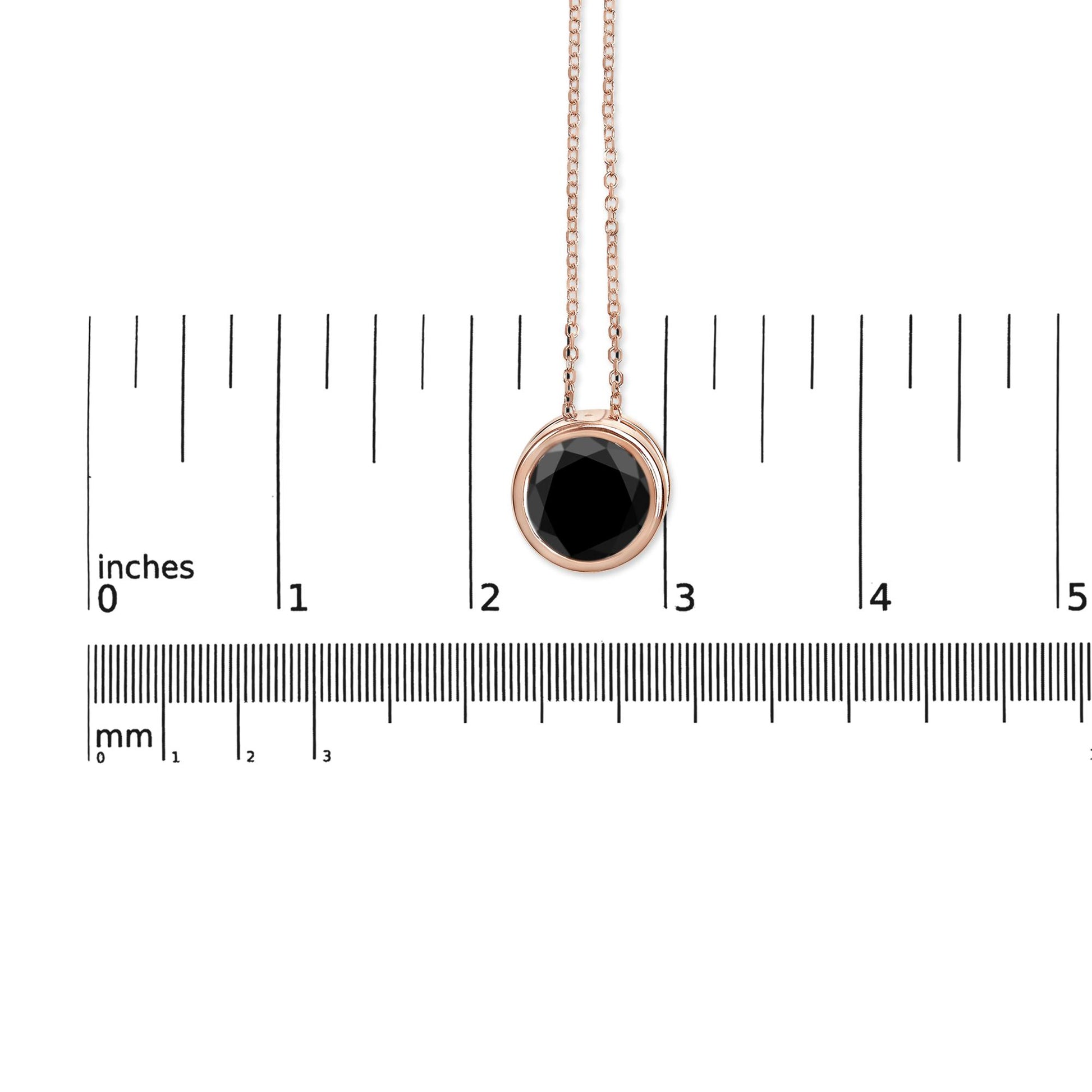 Rose metal necklace with a round black gemstone in bezel setting, shown hanging against a ruler for size reference, front view.