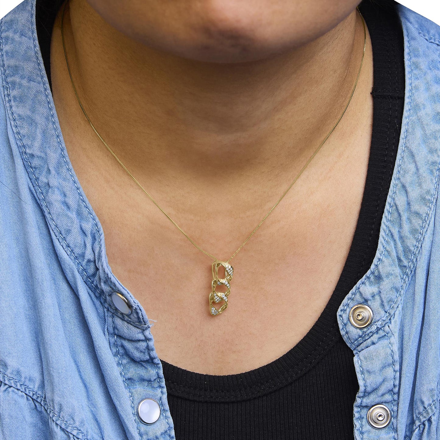 Close-up front view of a yellow metal necklace with a pendant featuring four linked sections adorned with multiple small white gemstones in prong settings, worn on a model dressed in a black top and light blue jacket.