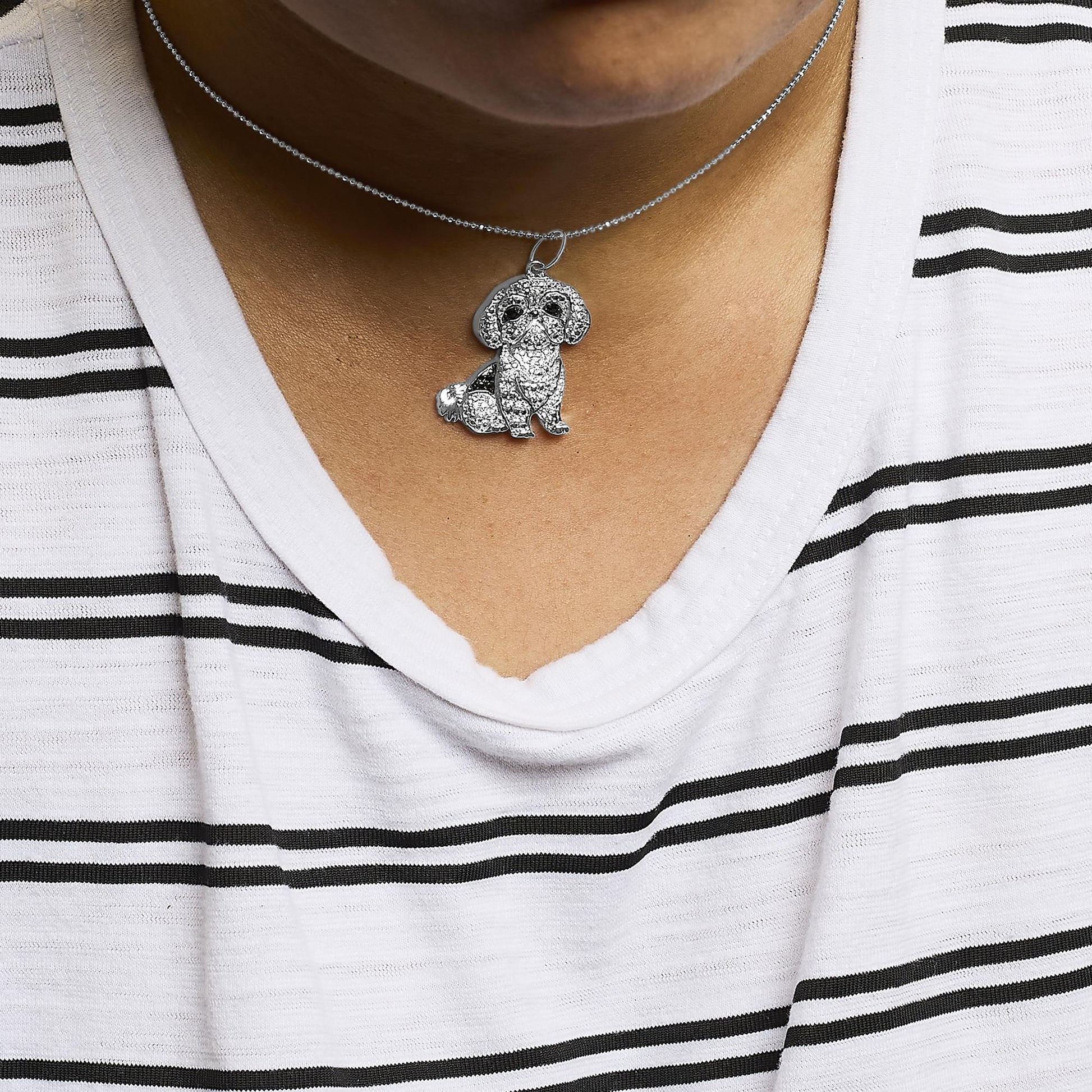 Close-up front view of a white metal necklace with a pendant shaped like a small dog, adorned with white and black round micro-pave set gemstones, worn on a model.
