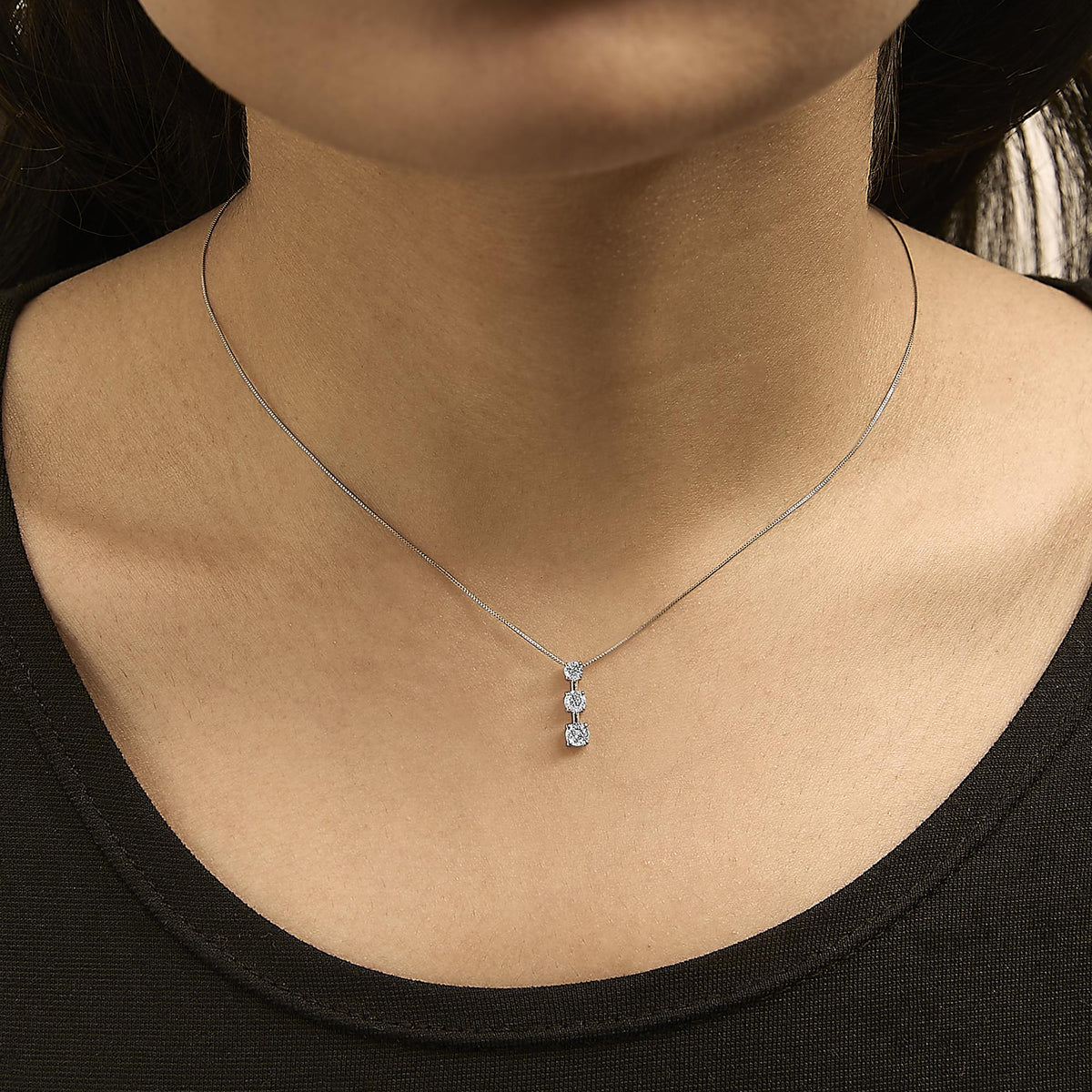 White metal necklace with three white gemstones in a vertical arrangement, shown worn on a model from a front angle.