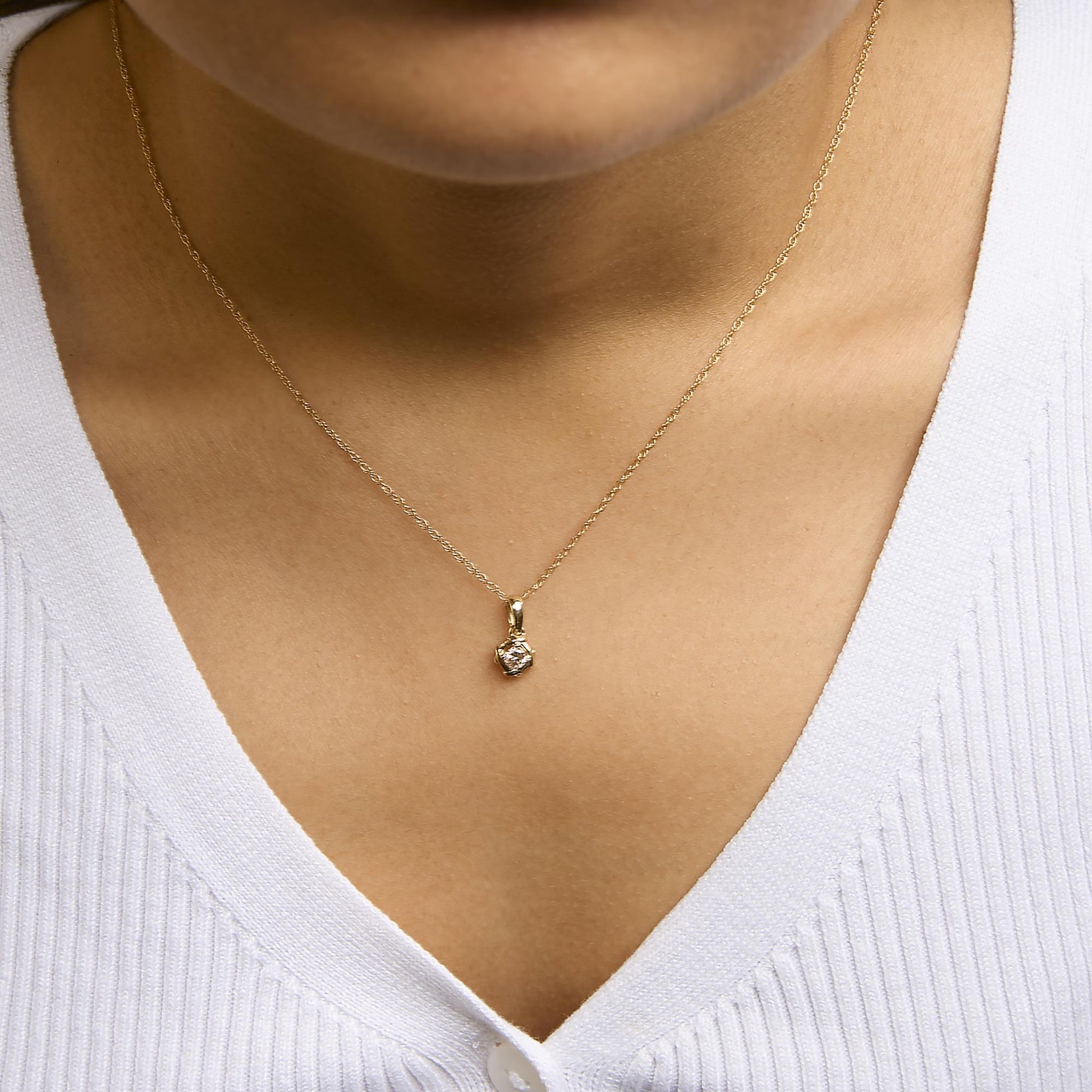 Close-up front view of a yellow metal necklace with a small round white gemstone in prong setting, shown worn on a model with a white top.