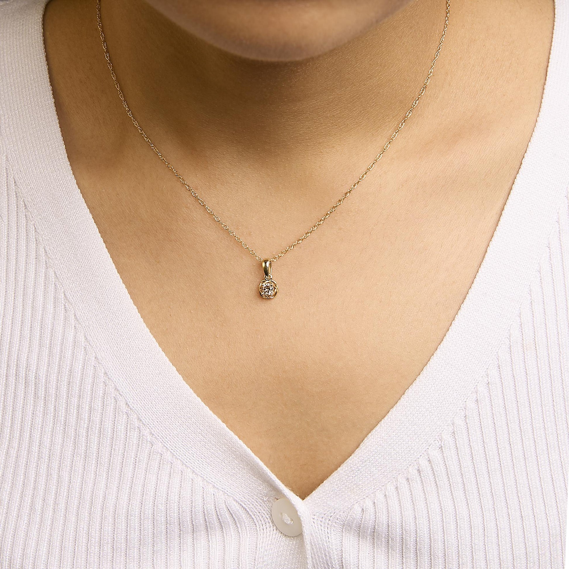 Close-up front view of a yellow metal necklace with a round white gemstone in a prong setting, shown worn on a model.