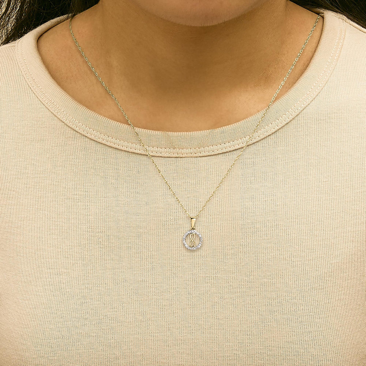Close-up front view of a model wearing a yellow metal necklace with a round pendant surrounded by white gemstones in a shared prong setting.