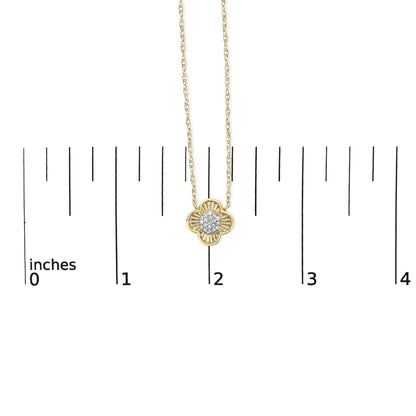 Yellow metal necklace with a clover-shaped pendant featuring round white gemstones in prong settings, shown on a ruler scale, front view.
