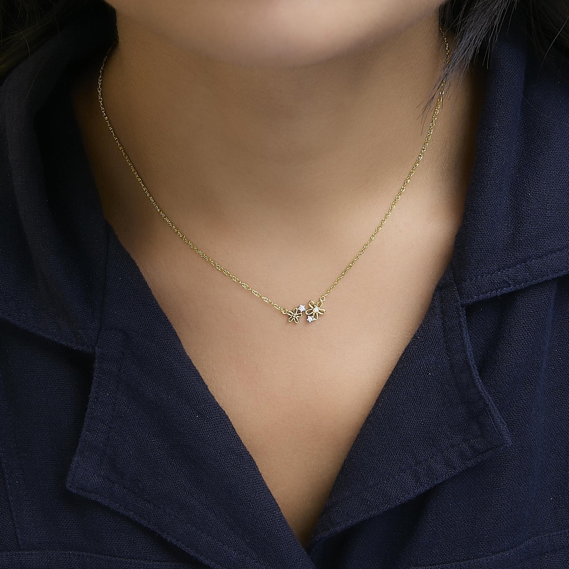 Yellow metal necklace with two small flower-shaped pendants, one with a single white gemstone and the other with two white gemstones, shown worn on a model in a close-up frontal shot.