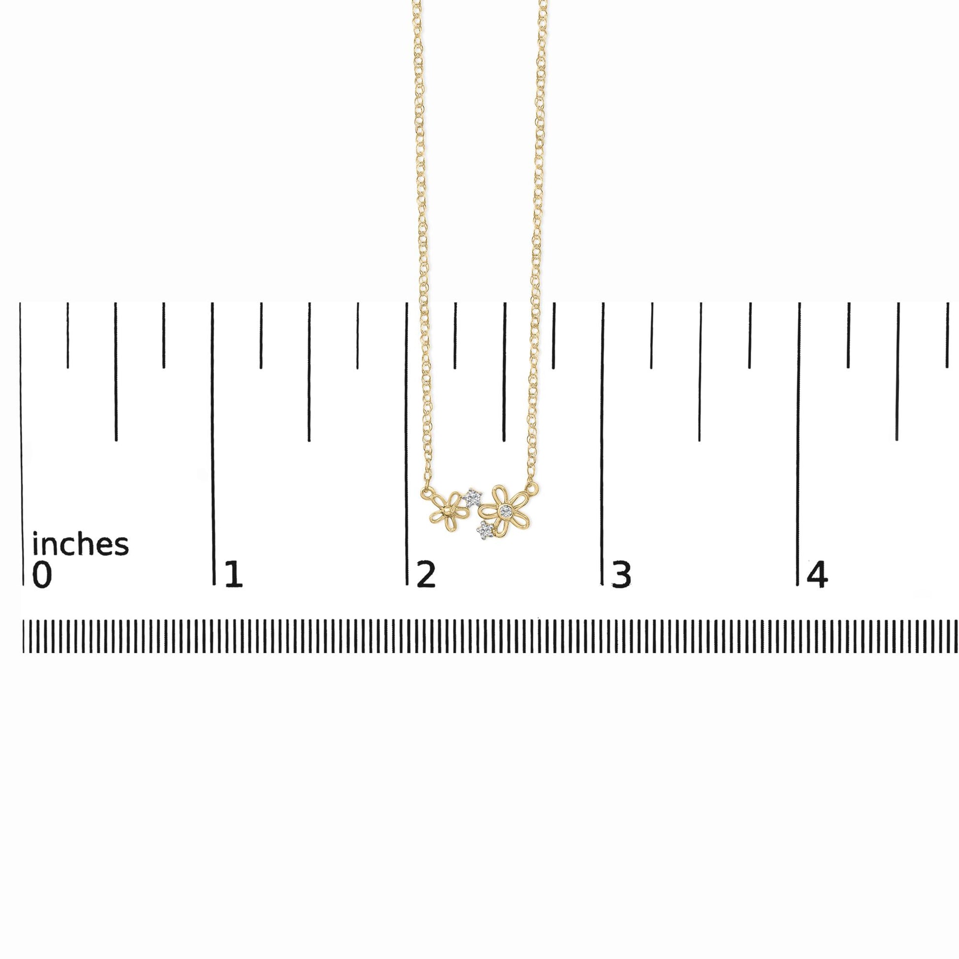 Yellow metal necklace with two open flower-shaped pendants each accented with small white gemstones, shown on a scale with a front-facing angle.