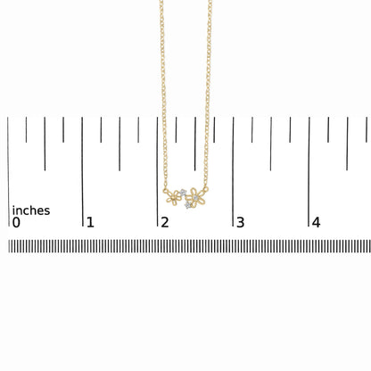 Yellow metal necklace with two open flower-shaped pendants each accented with small white gemstones, shown on a scale with a front-facing angle.