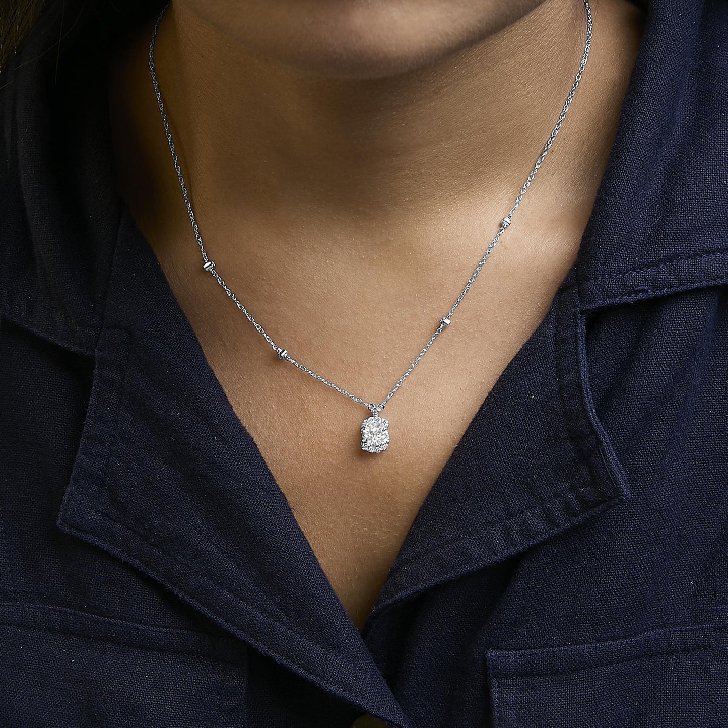 Necklace with white metal chain and multiple small white gemstones spaced along the chain, featuring a pendant with two larger round white gemstones, shown worn on a model from the front.