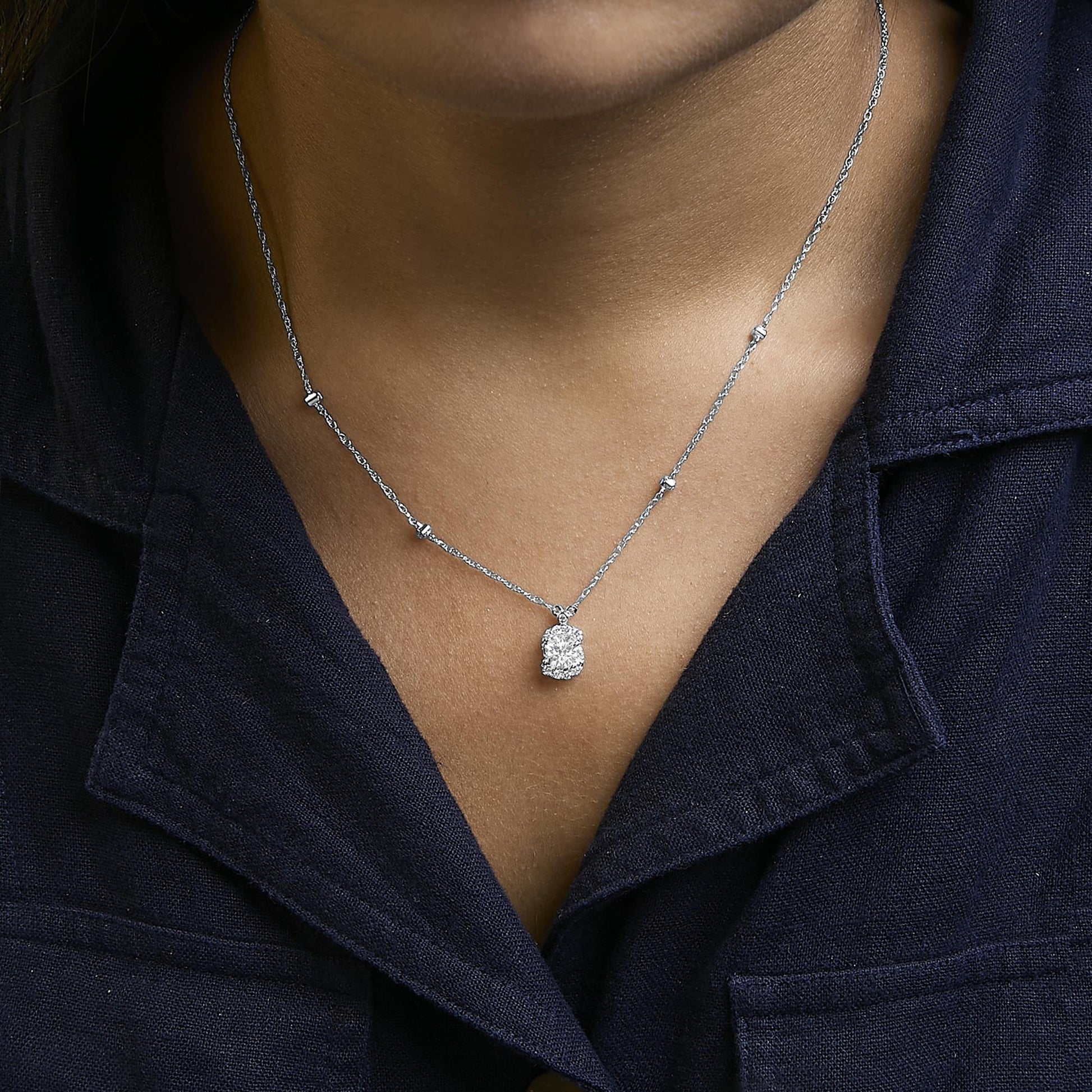 Necklace with white metal chain and multiple small white gemstones spaced along the chain, featuring a pendant with two larger round white gemstones, shown worn on a model from the front.
