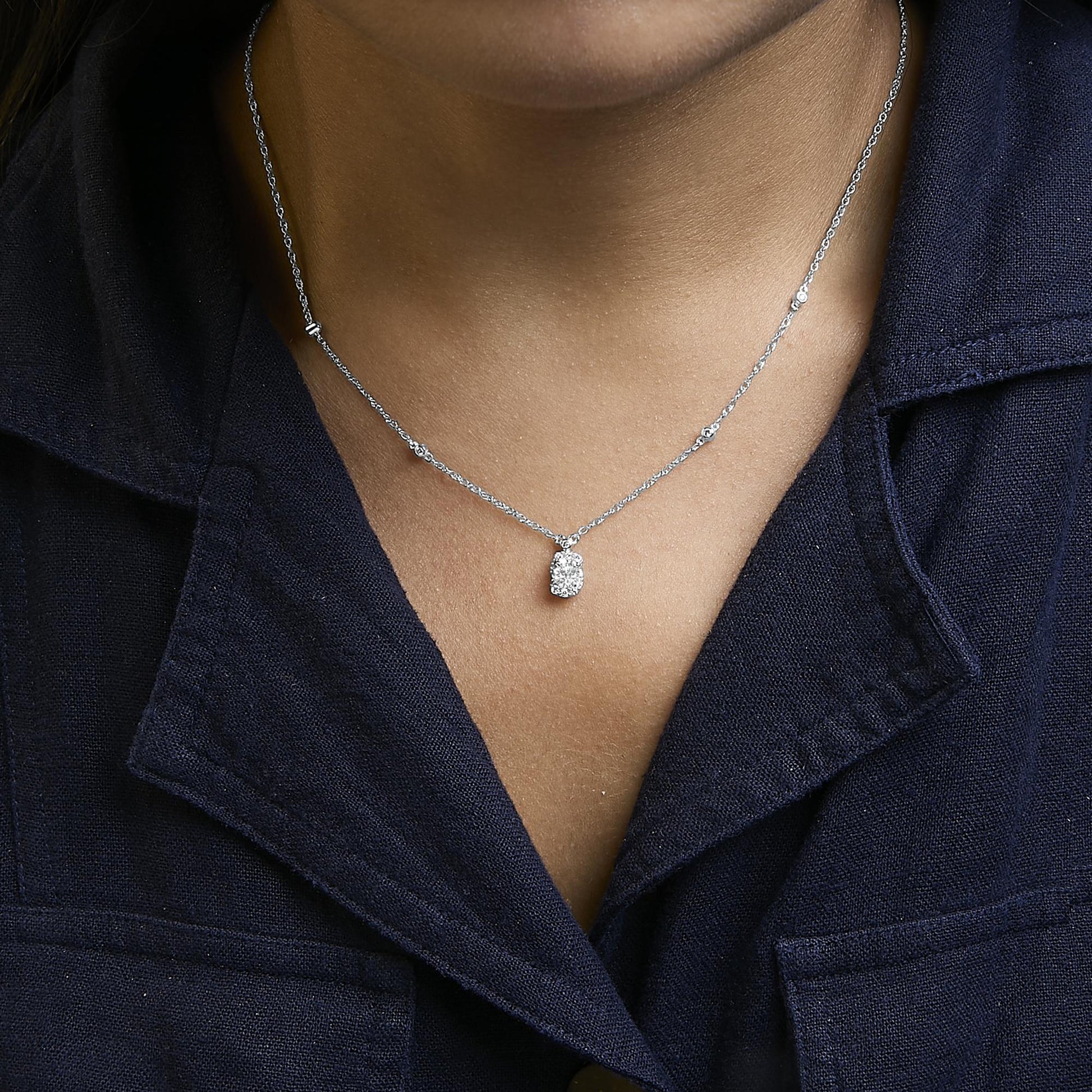 White metal necklace shown worn on a model, featuring a chain with small white gemstones set along it and a cushion-shaped pendant with multiple round white gemstones, shot from the front.