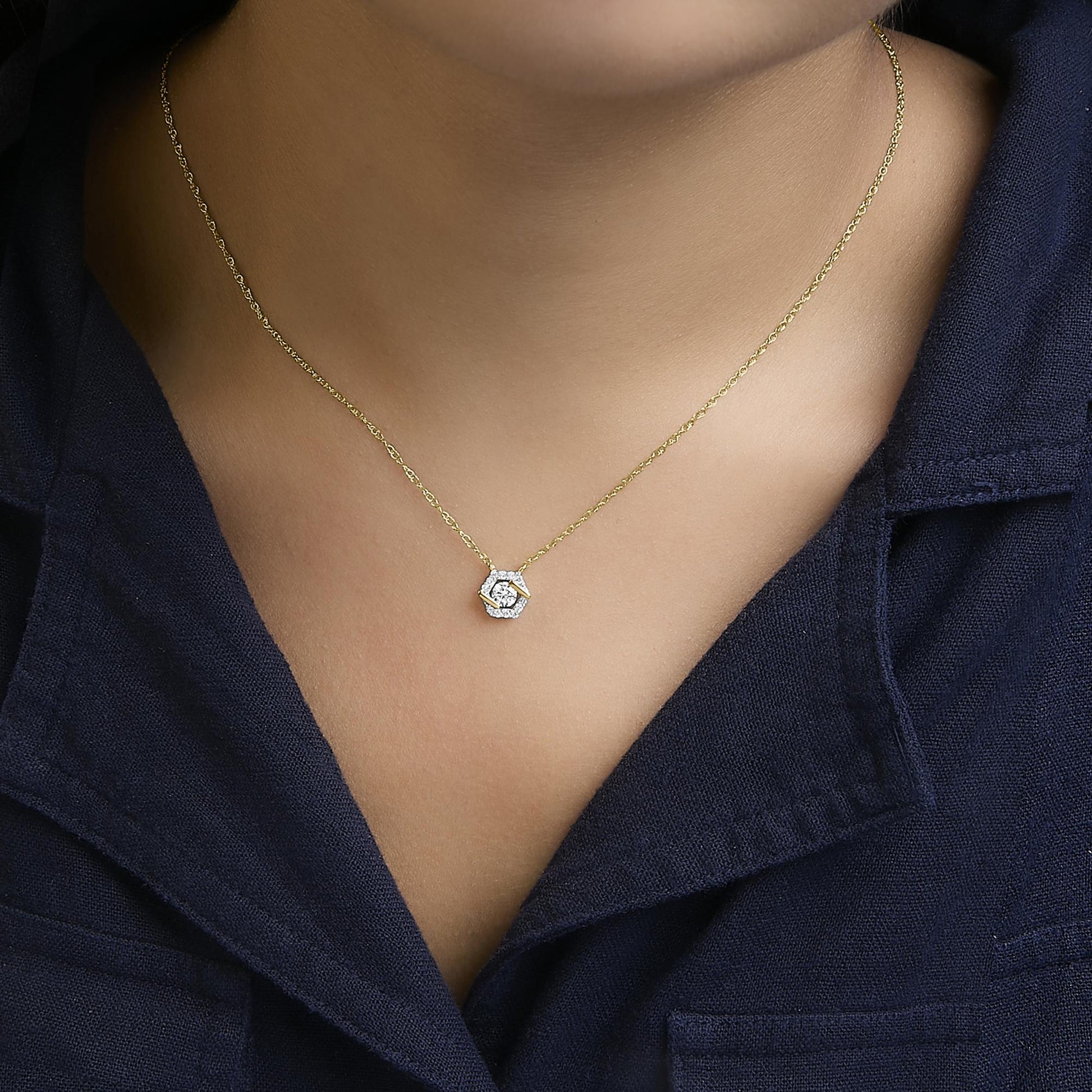 Close-up front view of a necklace with a yellow metal chain and a hexagonal pendant featuring white round gemstones in prong settings, worn by a model.