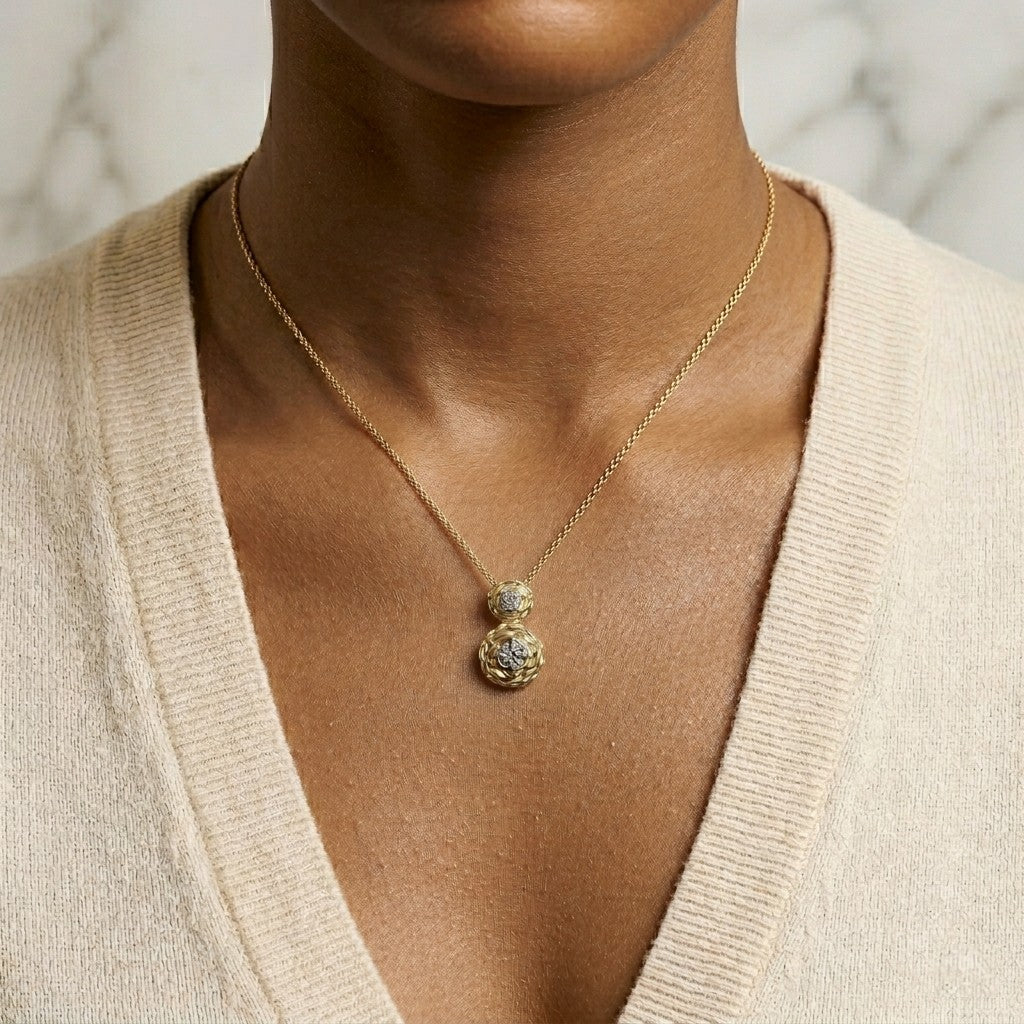 Yellow metal necklace with two round pendants, each featuring a white gemstone in a 4-prong setting, shown worn on a model from a front angle.
