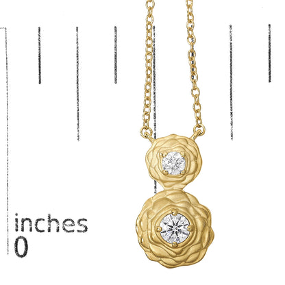 Close-up front view of a yellow necklace pendant with two round white gemstones in 4-prong settings, shown on a scale.