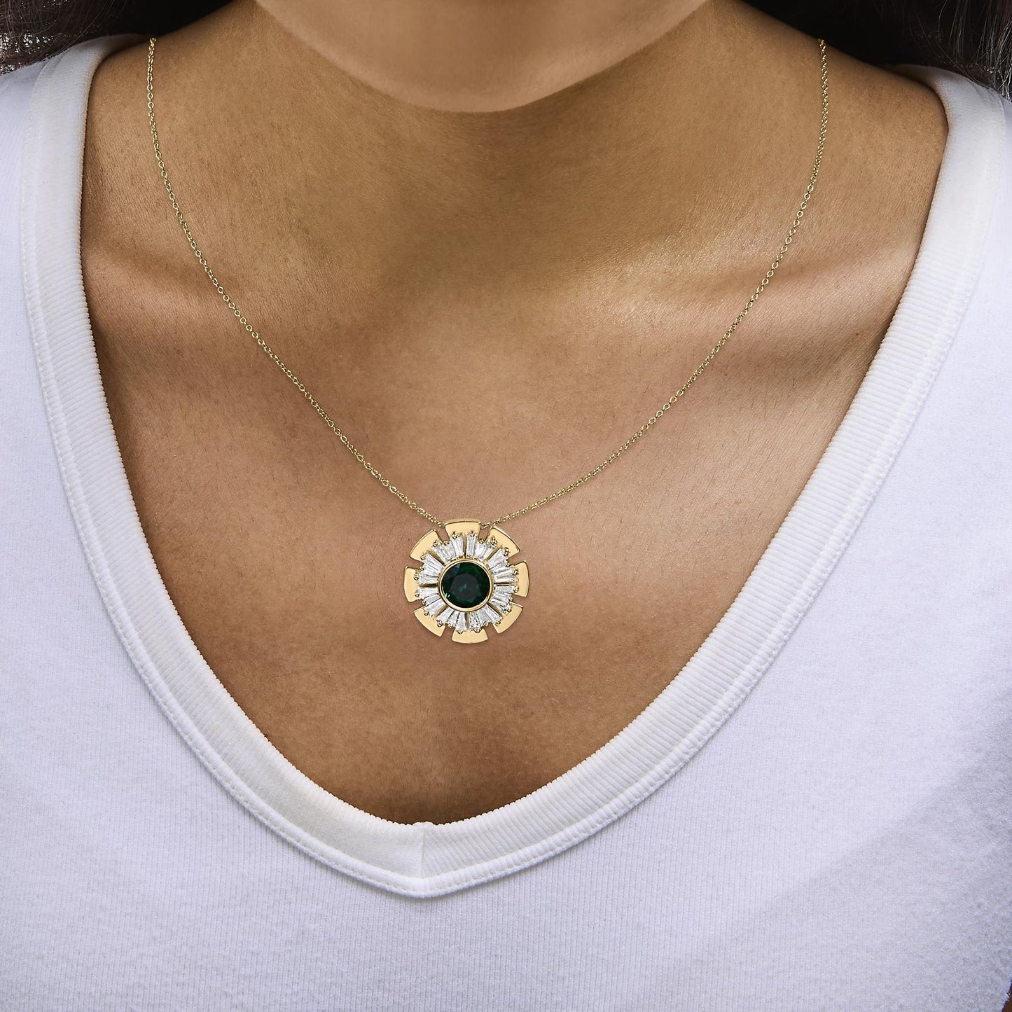 Close-up front view of a model wearing a yellow metal necklace with a round green gemstone center surrounded by white baguette-shaped gemstones in a prong setting.