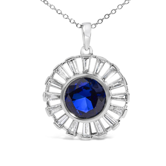 Close-up front view of a white metal necklace pendant featuring a large round blue gemstone bezel-set in the center, surrounded by a halo of white baguette-shaped gemstones in a channel setting, suspended from a delicate chain.