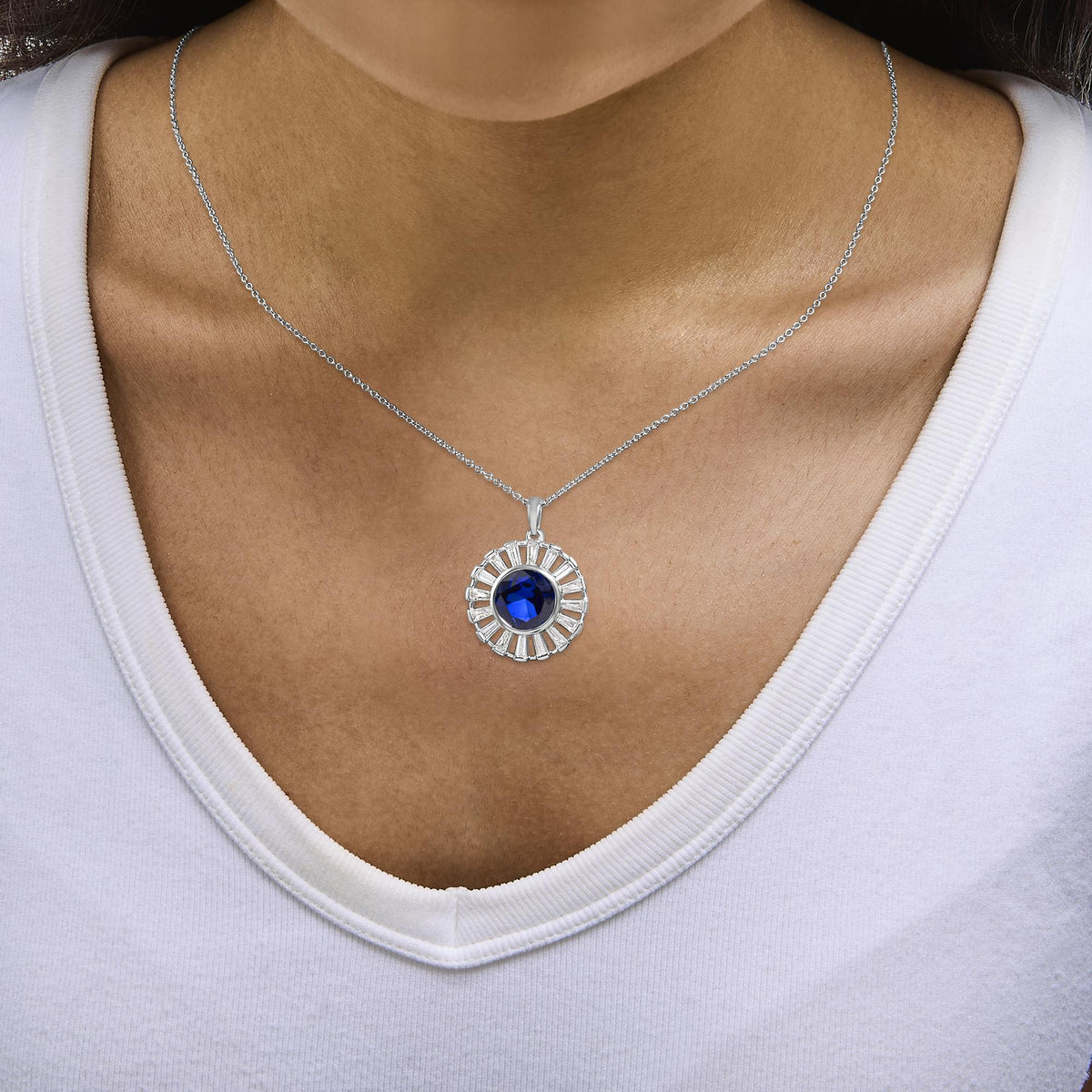 White metal necklace shown worn on a model, featuring a round blue gemstone center surrounded by white baguette-shaped gemstones in a circular design, shot from front angle.