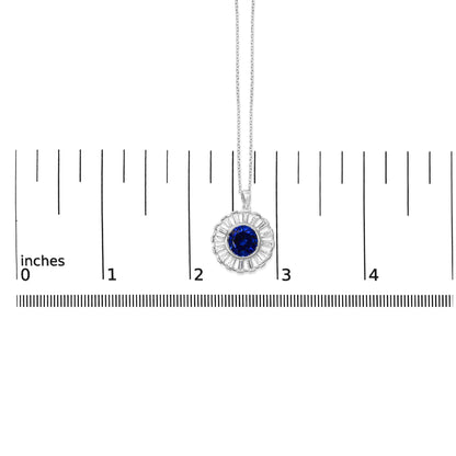 White metal necklace shown on a scale, featuring a circular pendant with a central round blue gemstone surrounded by baguette-shaped white gemstones in a channel setting. Shot is a close-up, front-facing view.