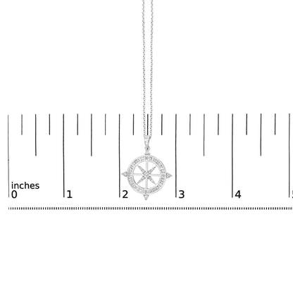 Close-up front view of a white metal necklace with a compass-shaped pendant. The pendant features a circular design with baguette-shaped white gemstones channel set around the outer edge and round white gemstones prong set within the compass points. The necklace is shown on a scale.