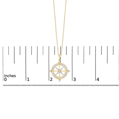 Yellow metal necklace with a round compass-shaped pendant featuring white baguette and round gemstones, shown on a scale with a front angle.