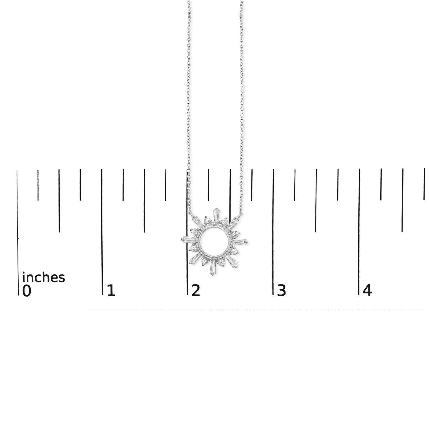 Close-up front view of a white metal necklace with a circular sunburst pendant featuring baguette and round white gemstones, shown on a ruler scale.