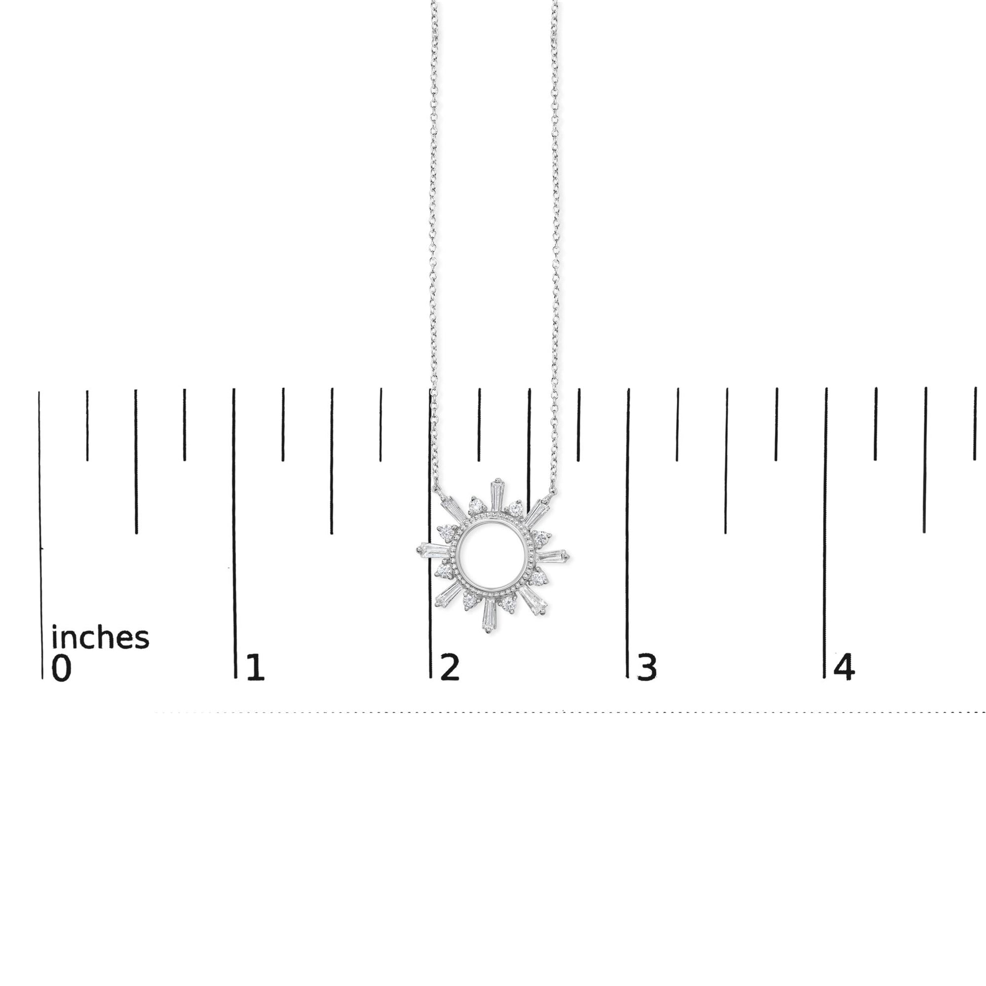 Close-up front view of a white metal necklace with a circular sunburst pendant featuring baguette and round white gemstones, shown on a ruler scale.