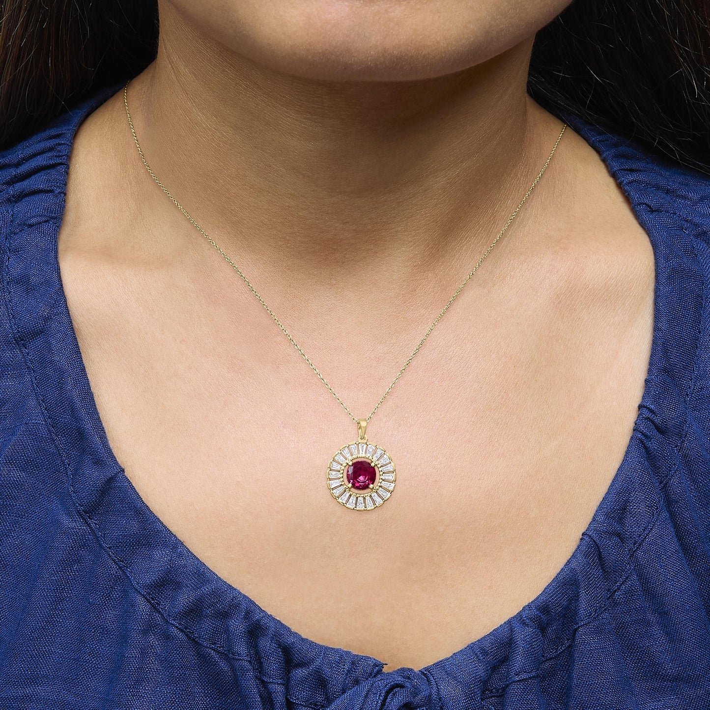 Yellow metal necklace with a round pendant featuring a central red gemstone surrounded by white baguette-shaped gemstones in a channel setting, shown worn on a model from the front angle.
