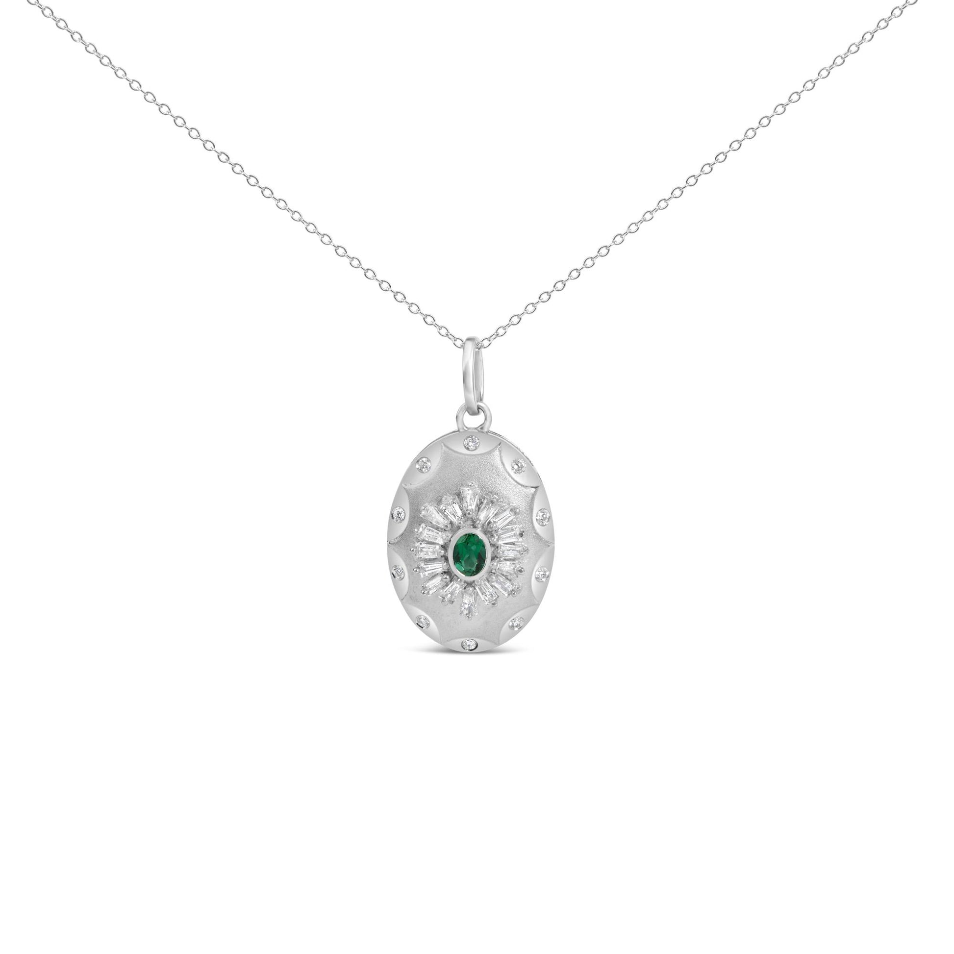 Close-up front view of a white metal necklace with an oval pendant featuring a central green gemstone surrounded by baguette and round white gemstones in prong and bezel settings.
