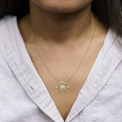 Close-up front angle of a yellow metal necklace with a circular pendant featuring prong-set white baguette and round gemstones, shown worn on a model.