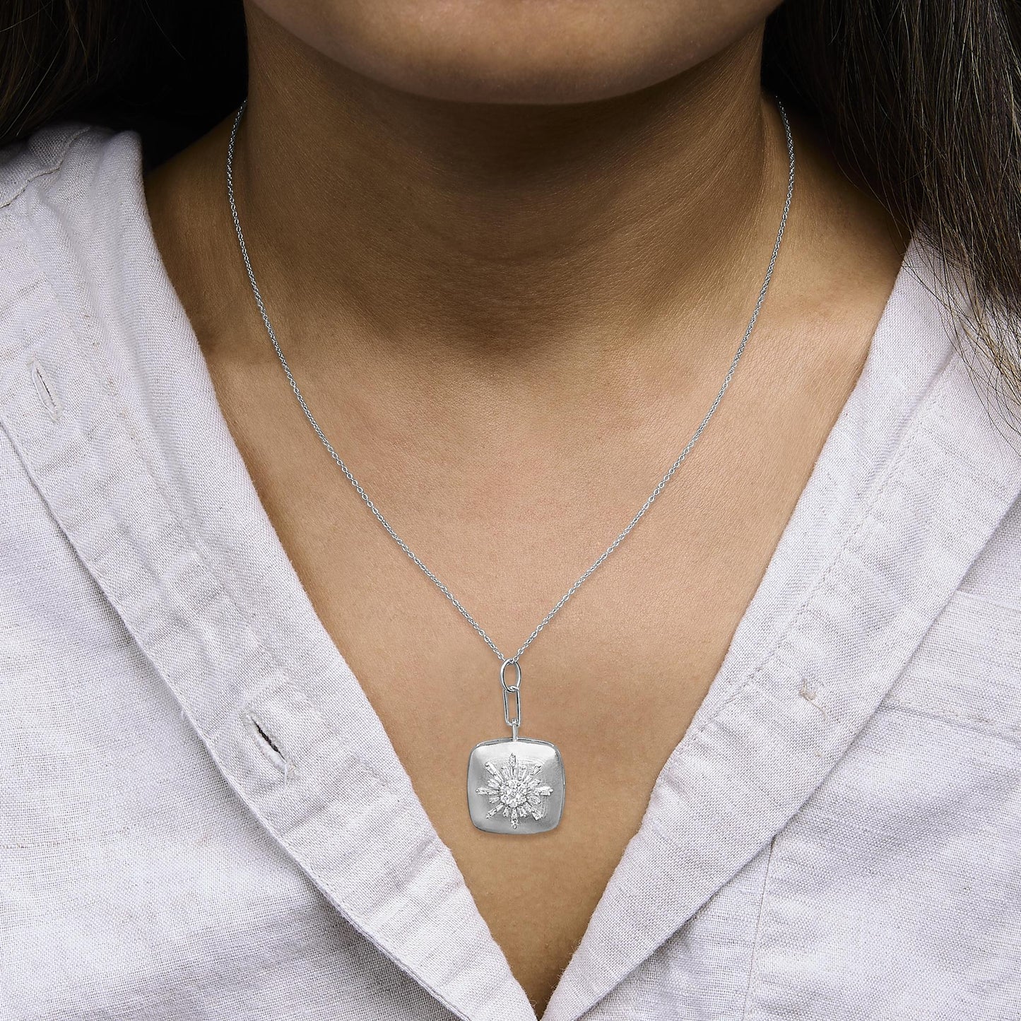 Close-up front view of a model wearing a white metal necklace with a rectangular pendant featuring a cluster of white baguette and round prong-set gemstones in a starburst pattern.