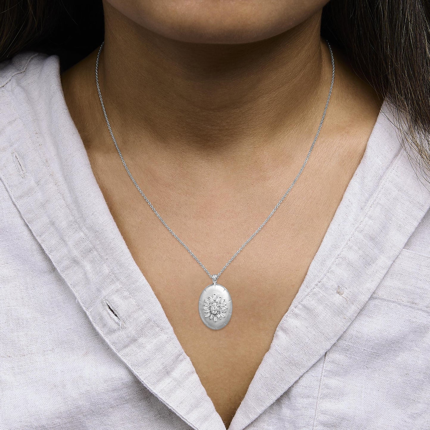White metal necklace shown worn on a model, featuring an oval pendant with round and baguette-shaped white gemstones in prong settings, photographed from a front close-up angle.