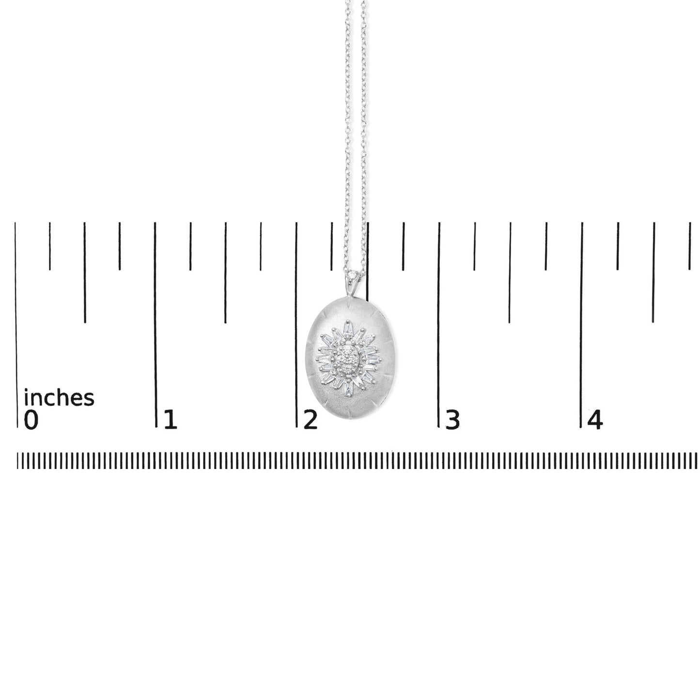 Close-up front view of a white metal necklace pendant with an oval shape, featuring a central cluster of prong-set white baguette and round gemstones, shown against a ruler scale for size reference.