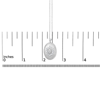 Close-up front view of a white metal necklace pendant with an oval shape, featuring a central cluster of prong-set white baguette and round gemstones, shown against a ruler scale for size reference.
