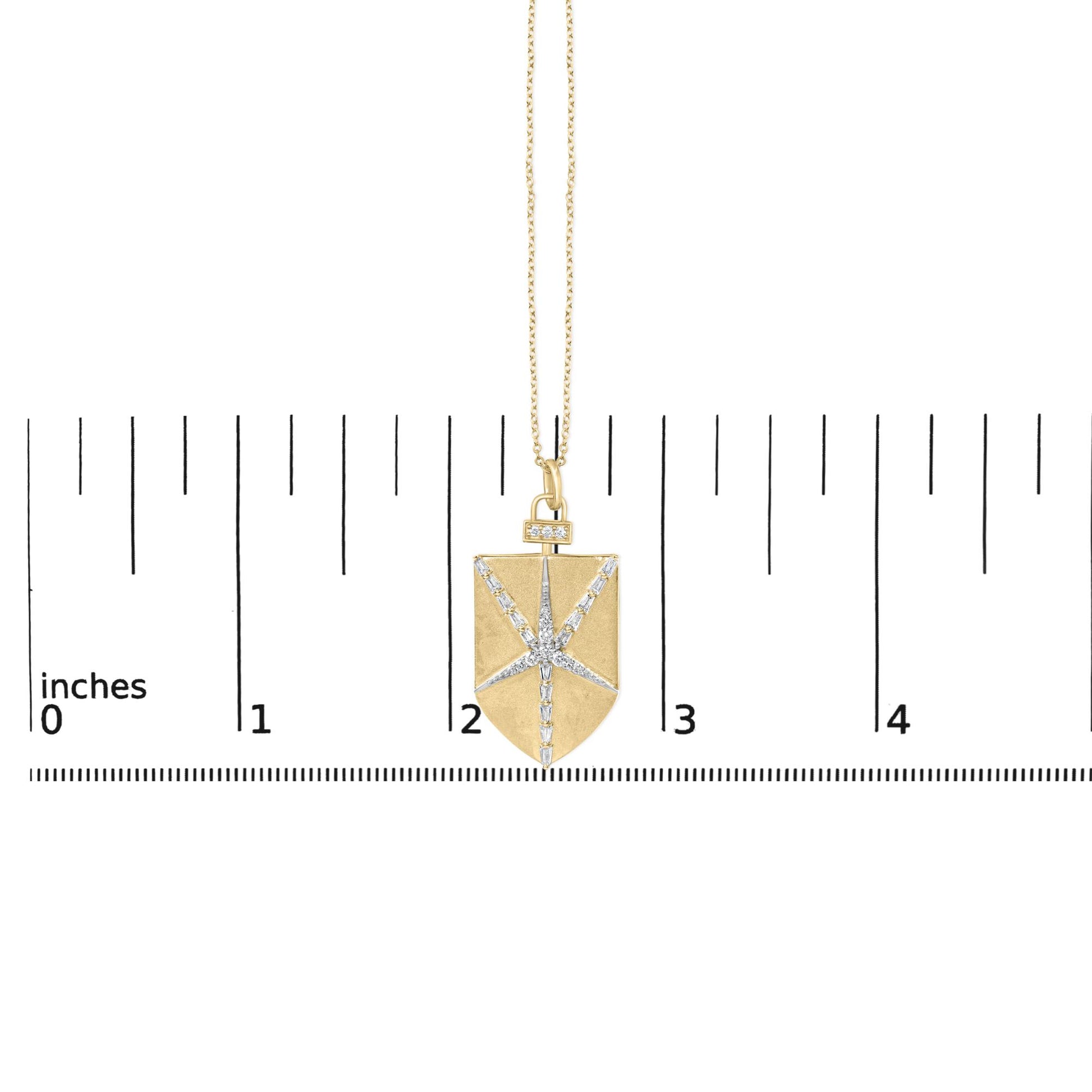 Close-up image of a yellow necklace pendant with a rectangular shape featuring white round and baguette gemstones arranged in a starburst pattern, shown on a scale.