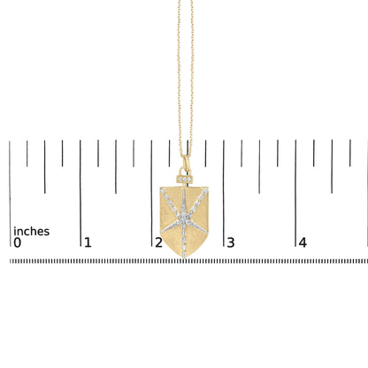 Close-up image of a yellow necklace pendant with a rectangular shape featuring white round and baguette gemstones arranged in a starburst pattern, shown on a scale.