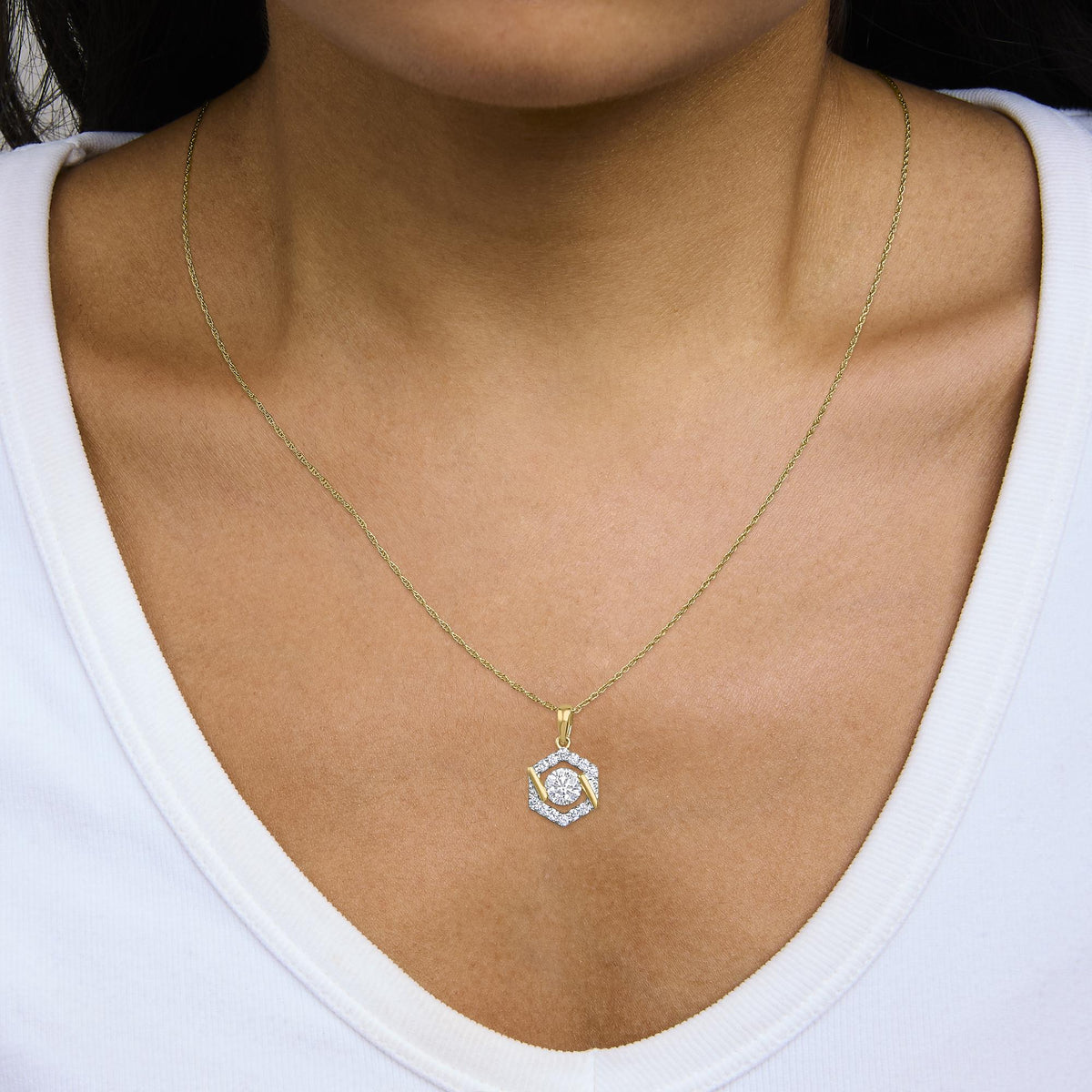Close-up front view of a yellow metal necklace with a hexagonal pendant adorned with a central round white gemstone surrounded by smaller white gemstones, shown worn on a model.