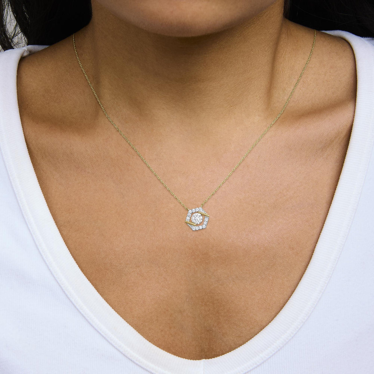 Close-up front view of a model wearing a yellow metal necklace with a hexagonal pendant featuring white round gemstones in prong settings.