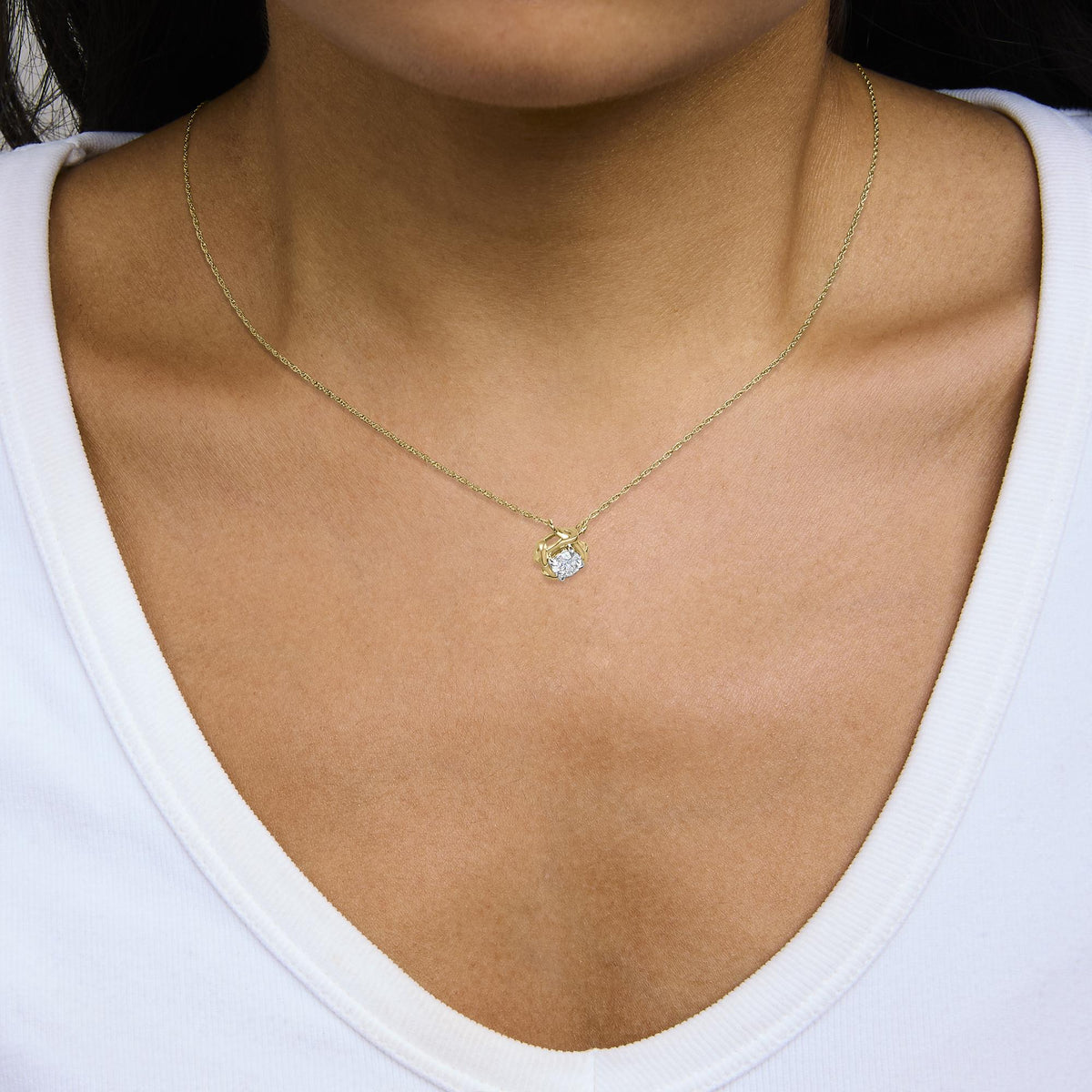 Close-up front view of a model wearing a yellow metal necklace with a round white gemstone in a prong setting pendant.